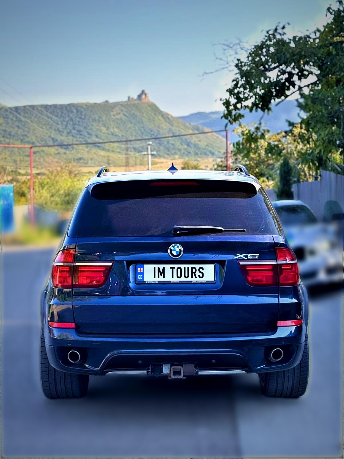 Our blue BMW X5 on a road in Mtskheta, with Jvari Monastery on the mountain behind it